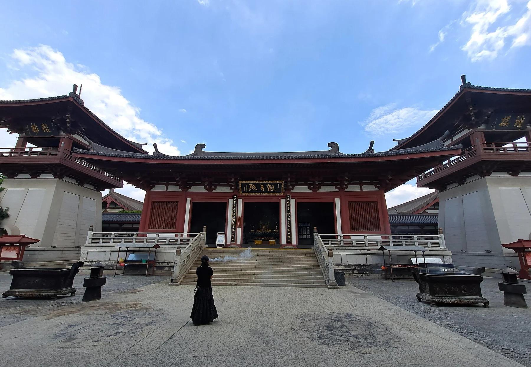 Broad pale paving between red-columned, tiled-roof temple halls.