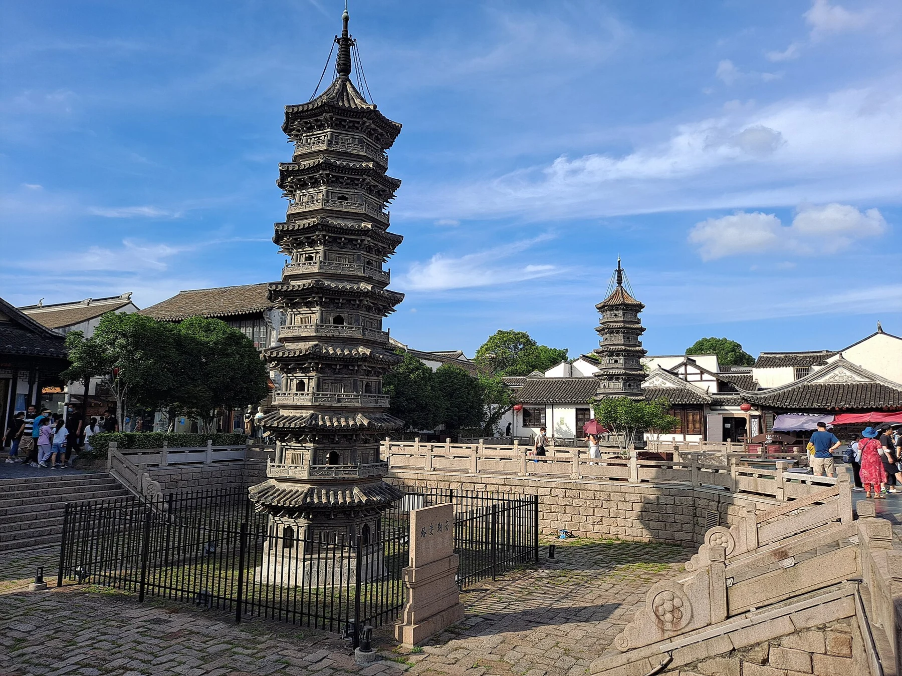A small seven-tiered brick tower in the foreground and its paired tower farther away.