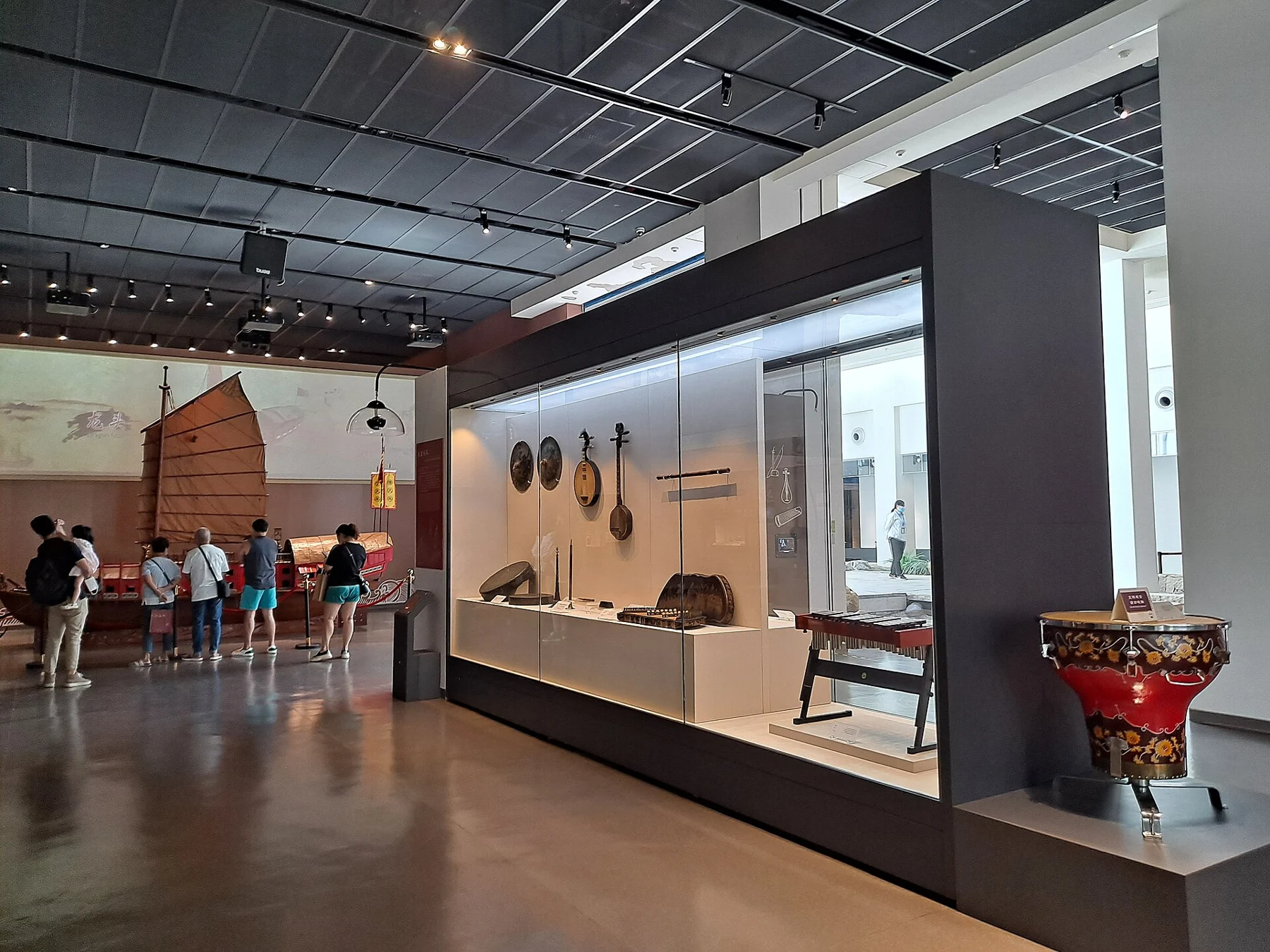 Instruments in a museum display case, a drum at right and a red-hulled boat model at left