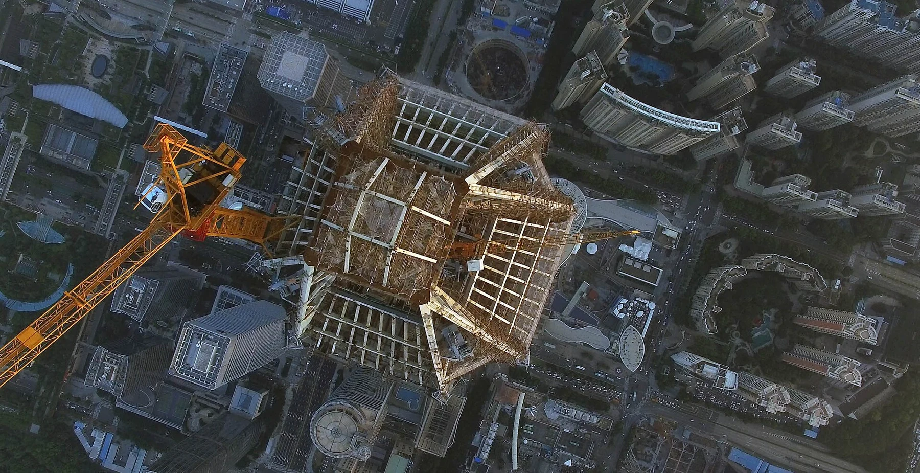 Construction cranes and an unfinished tower crown high above dense city blocks.