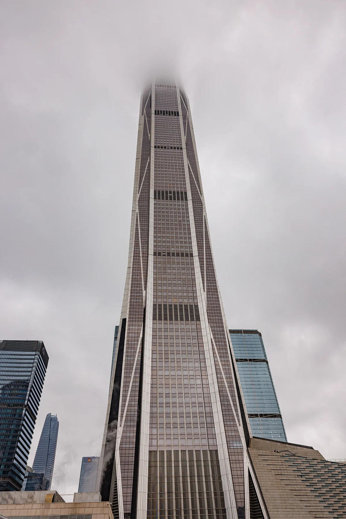 The tapering tower rises from nearby buildings, with its upper crown obscured by cloud.