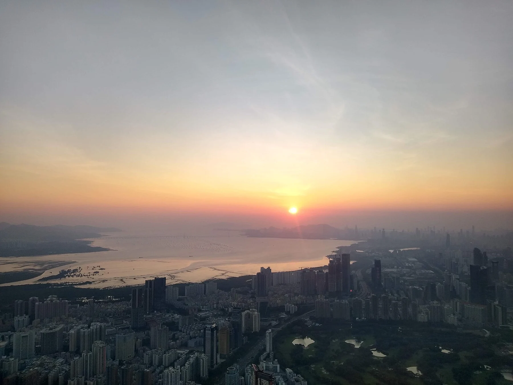 Orange sun above water, with city towers dark in the foreground.