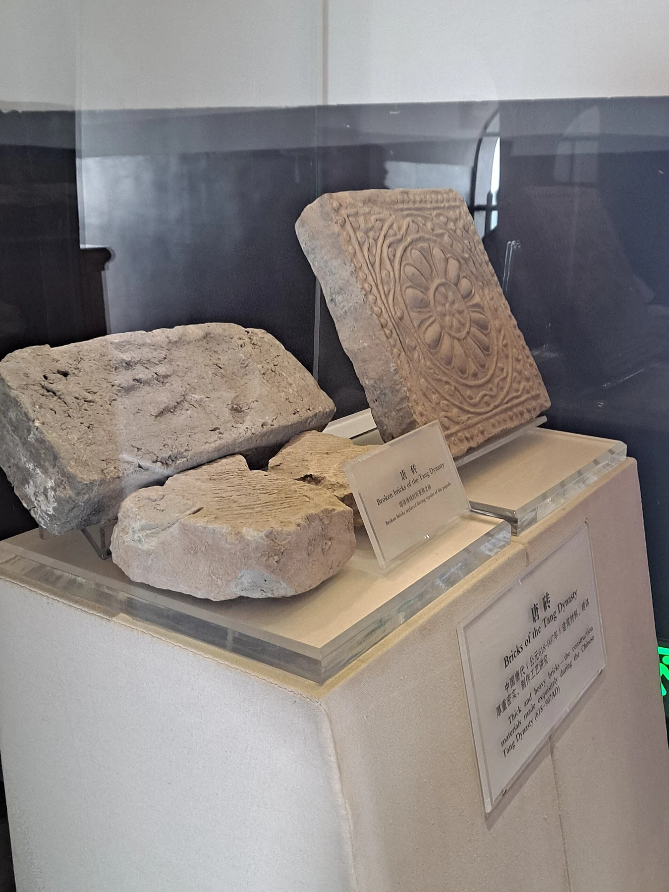 Broken brick fragments and a decorated square brick behind a glass display case.