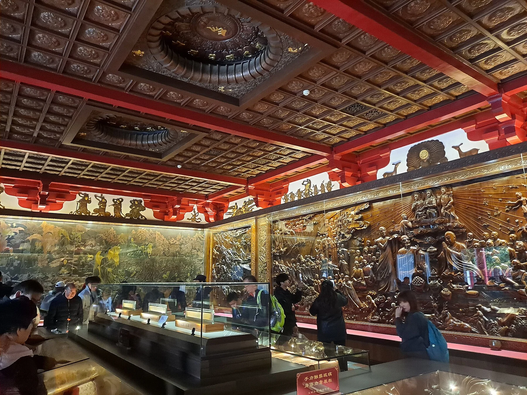Visitors, display cases and narrative relief decoration inside the temple memorial setting.