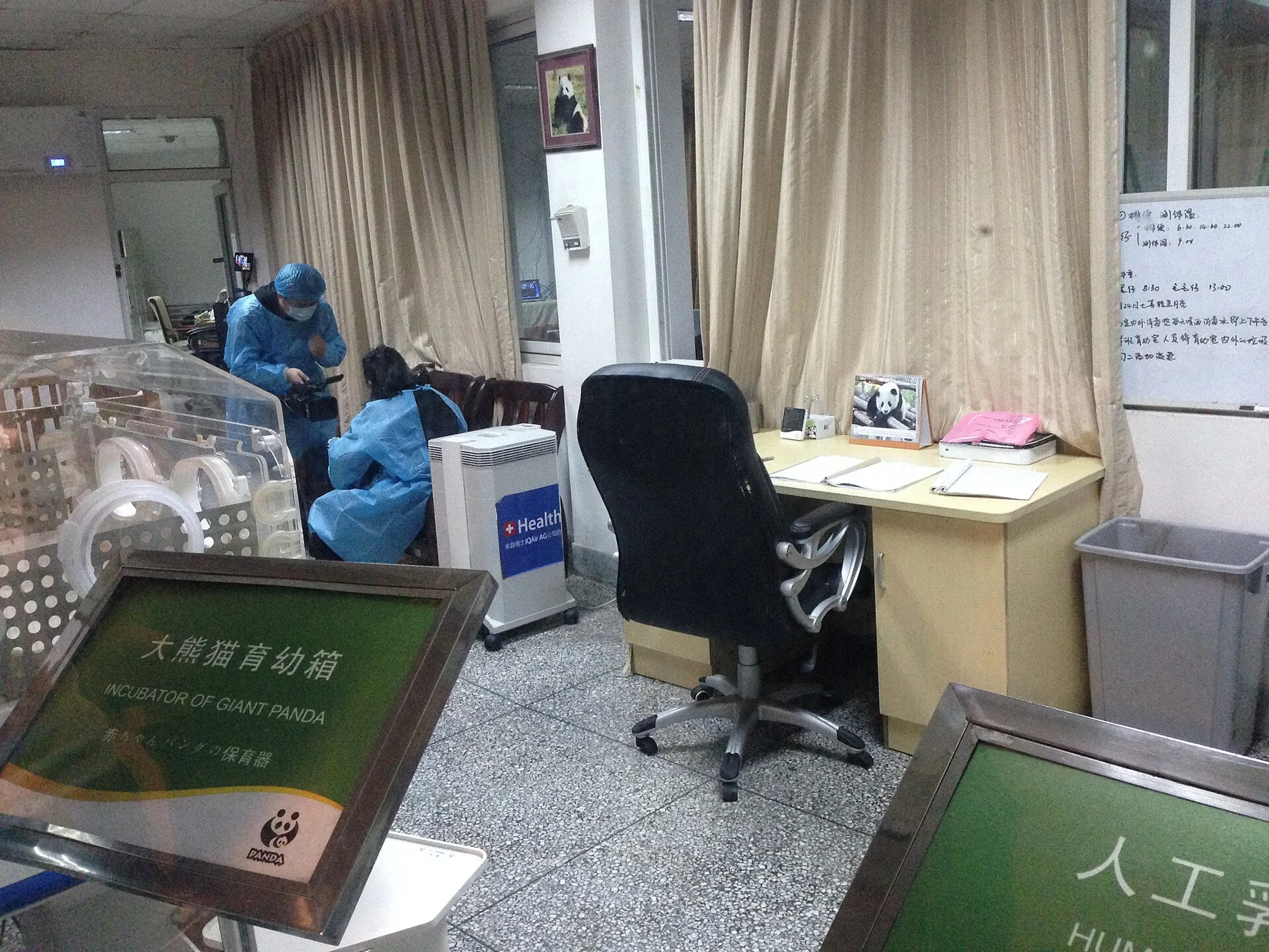 Glass-fronted view into a room with incubator equipment and two staff figures