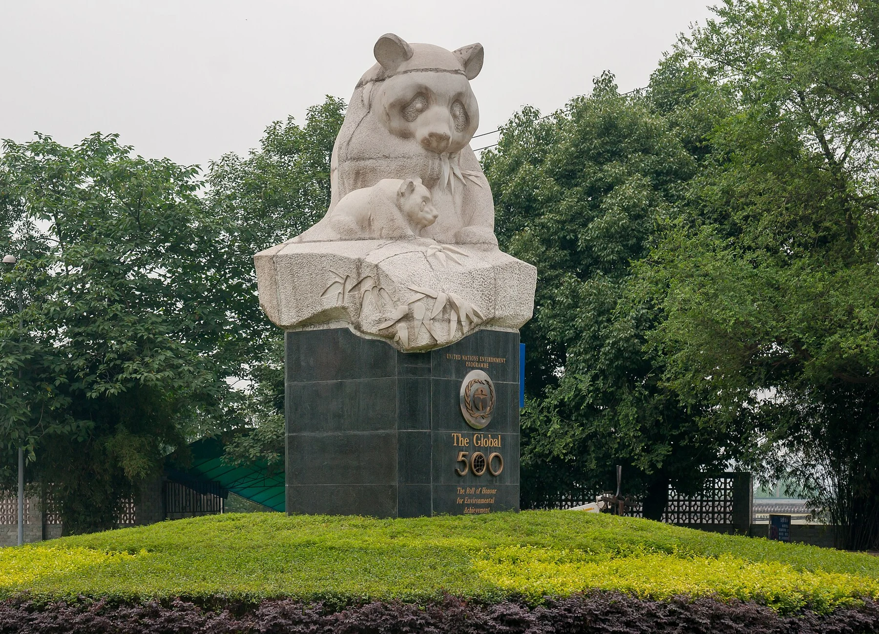 Stone sculpture of pandas on a pedestal surrounded by plants