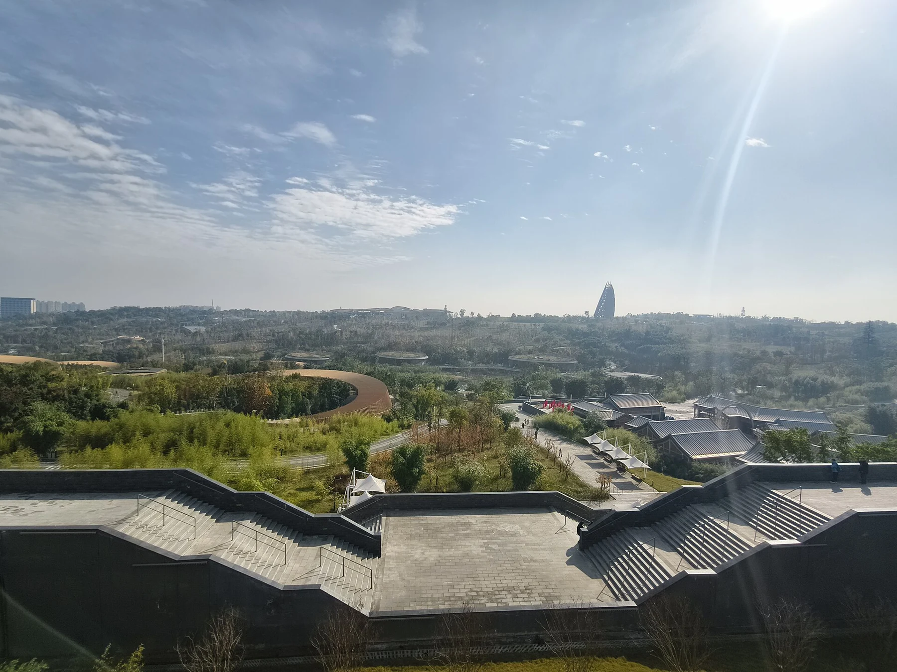 Elevated view over planted grounds, low roofs and distant landscape under a bright sky