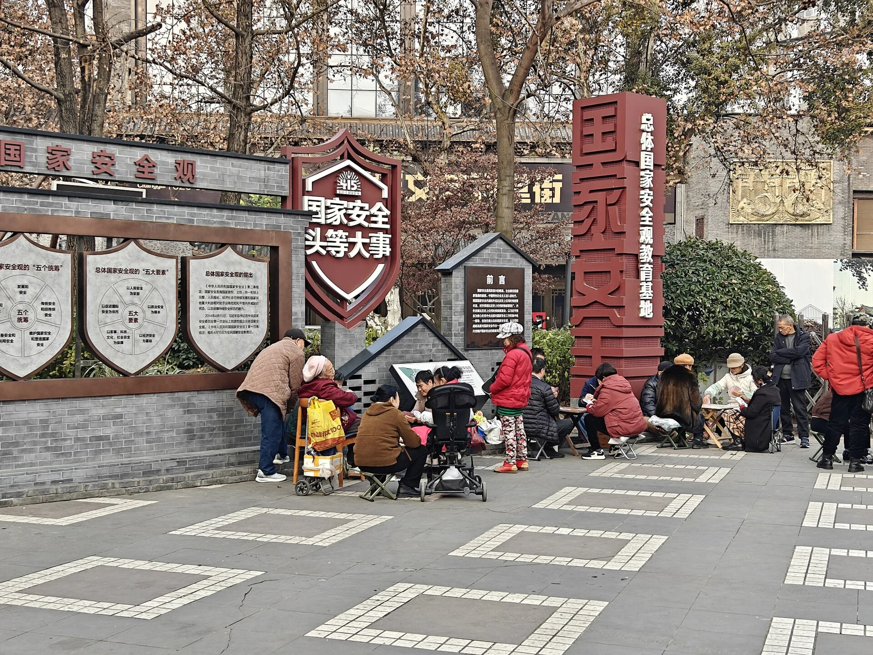 People sitting around tables playing cards beside a tree-lined path.
