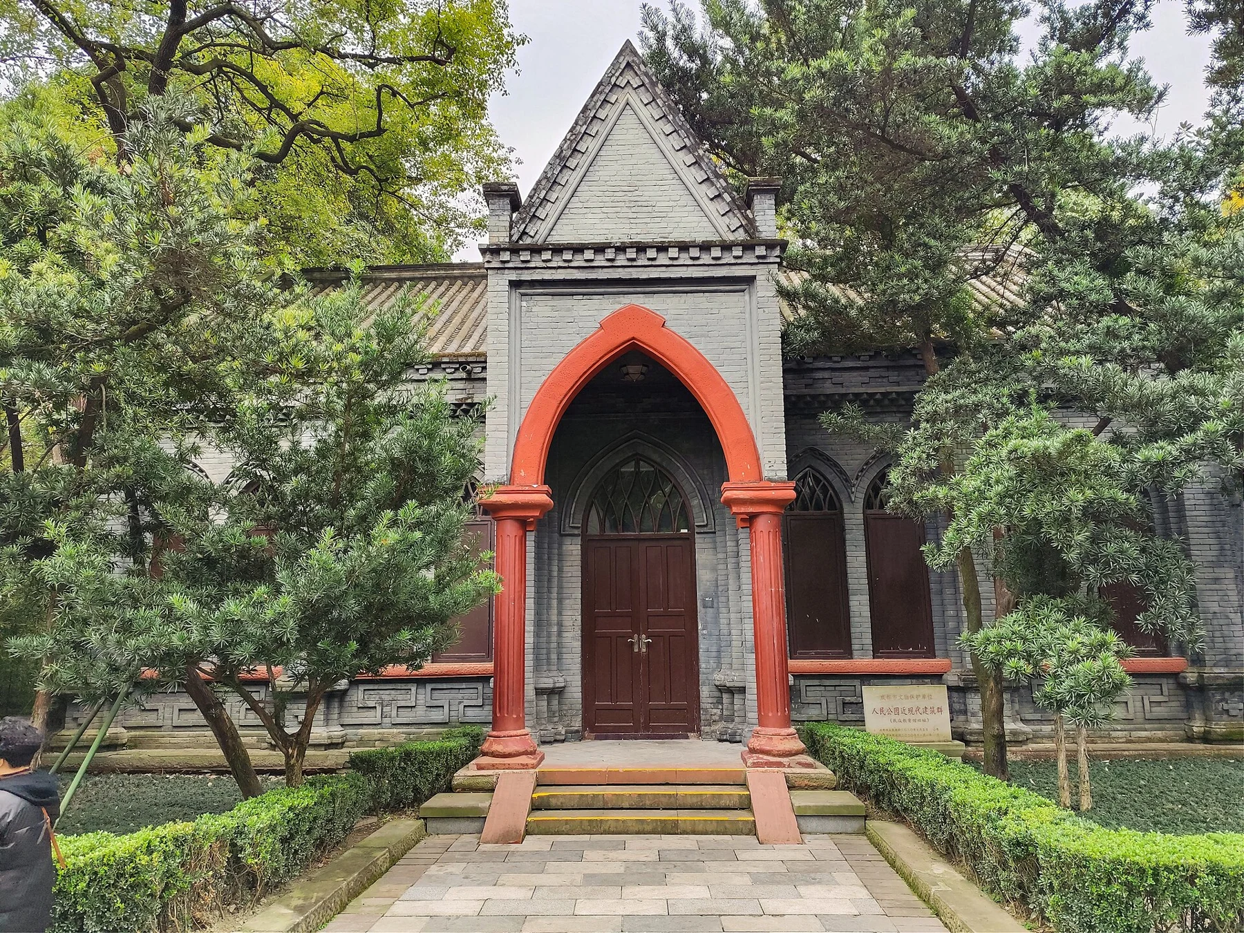 A grey-brick gabled facade with a pointed red-orange arch around a closed wooden doorway.
