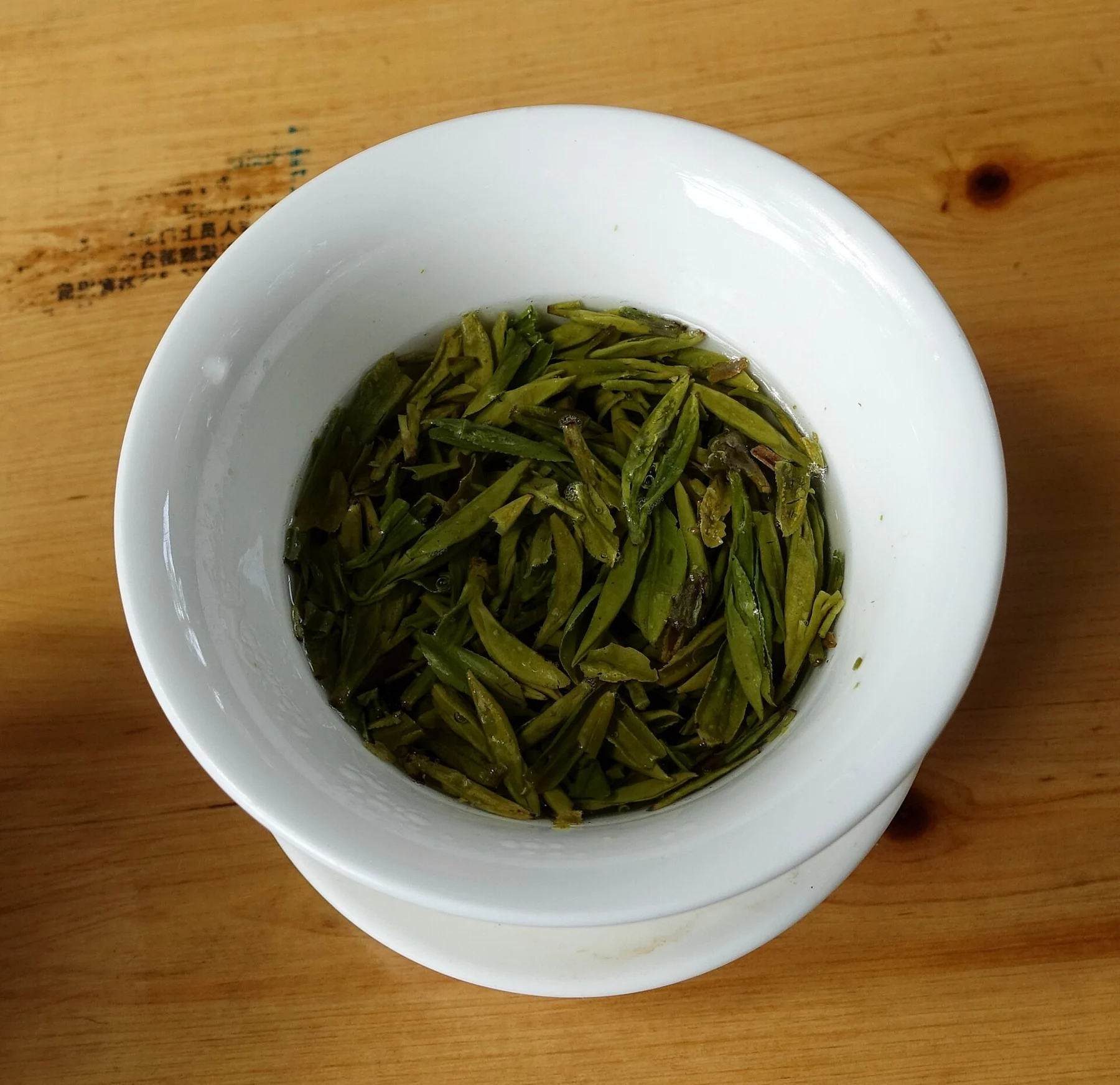 Loose tea leaves steeping in a white bowl on a wooden table.