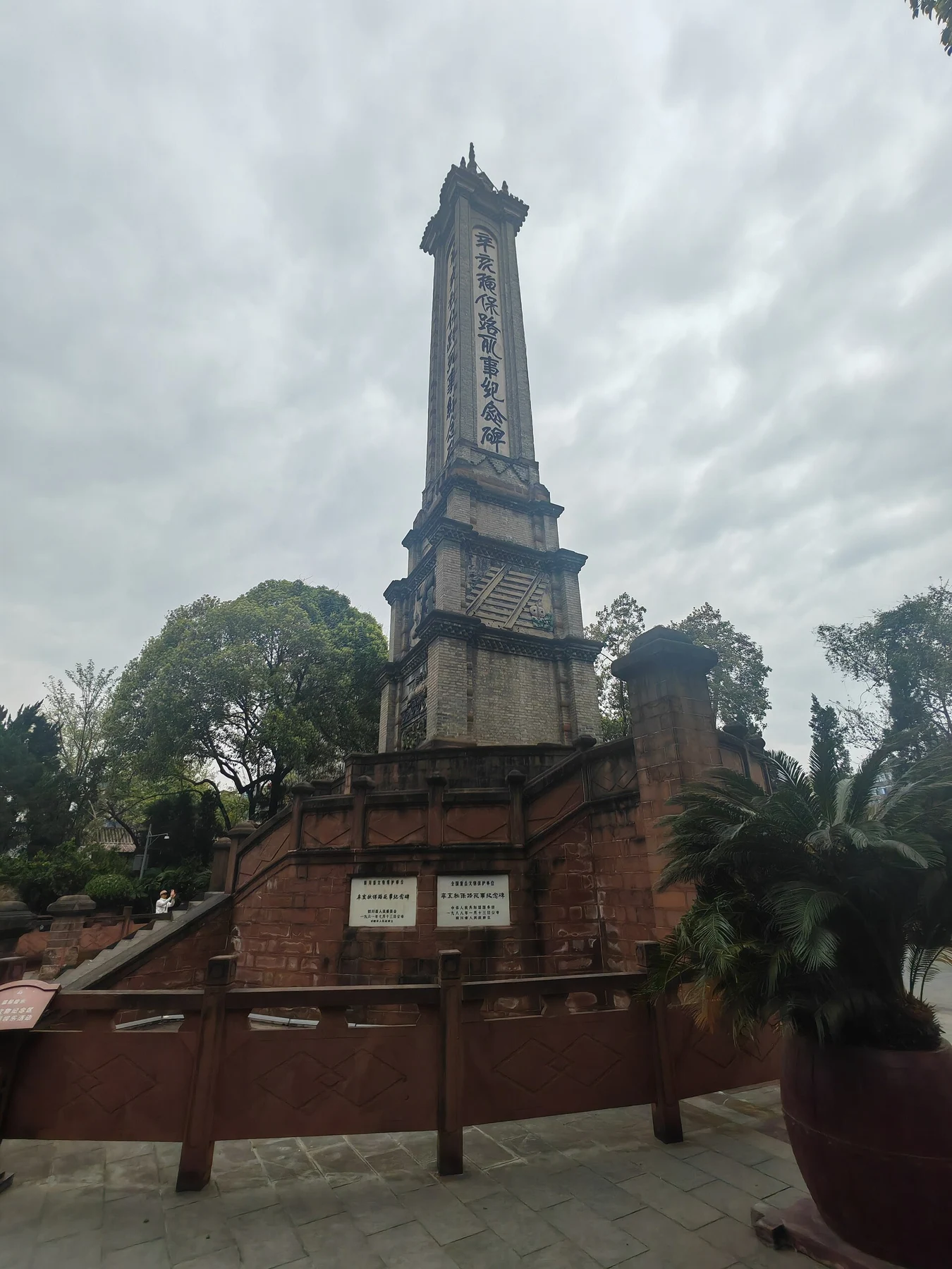 The memorial tower rising above a raised red-brown base beneath an overcast sky.