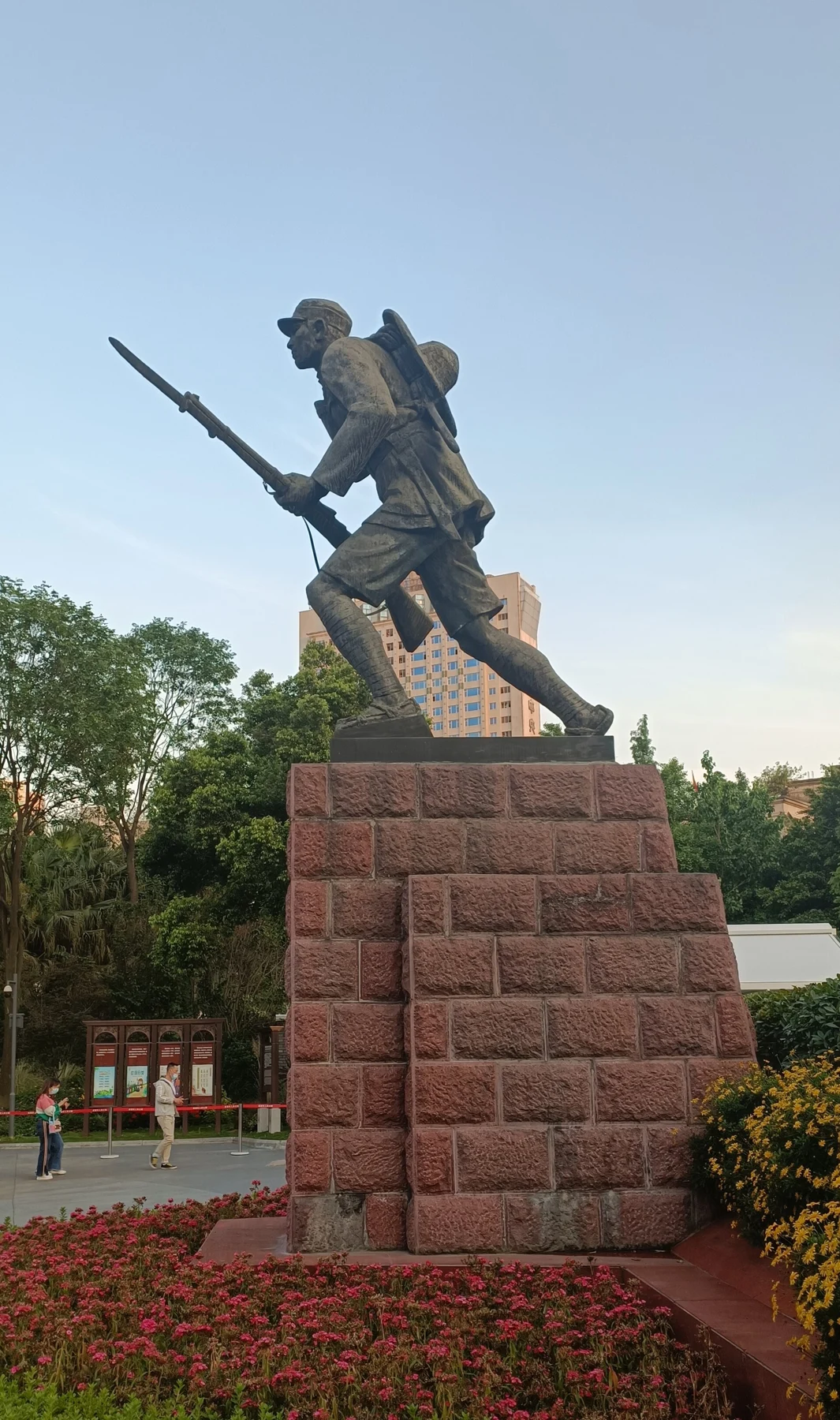Side view of a bronze soldier carrying a rifle and pack, mounted on a stone pedestal.