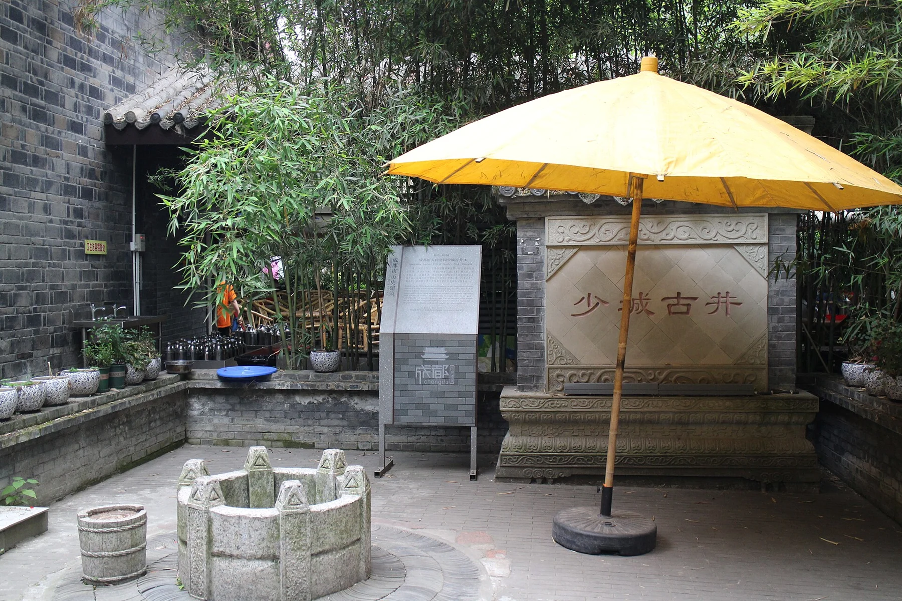 A small stone wellhead beside a Shaocheng old-well inscription and a yellow parasol.