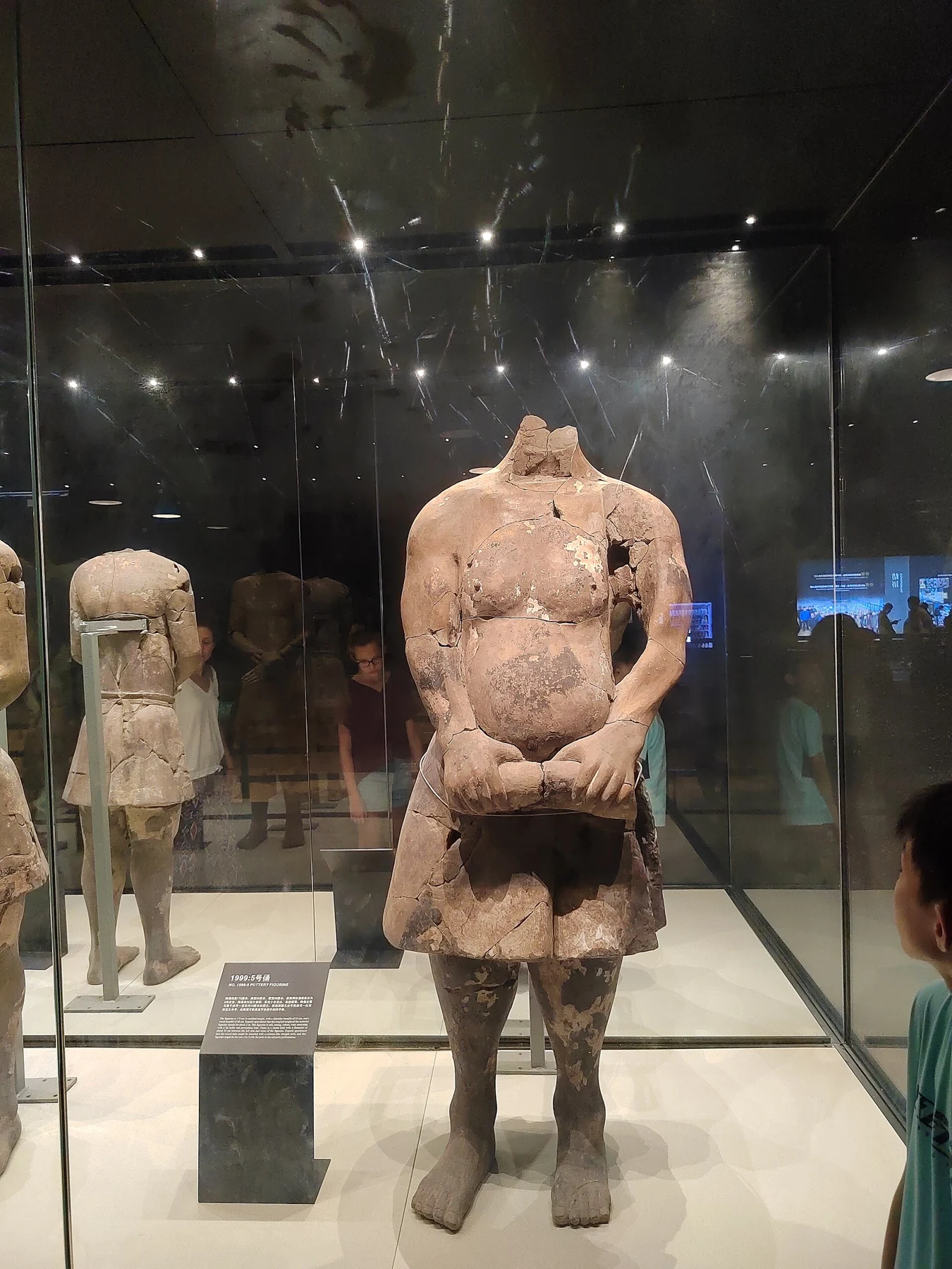 A headless acrobat-type terracotta figure displayed in a case