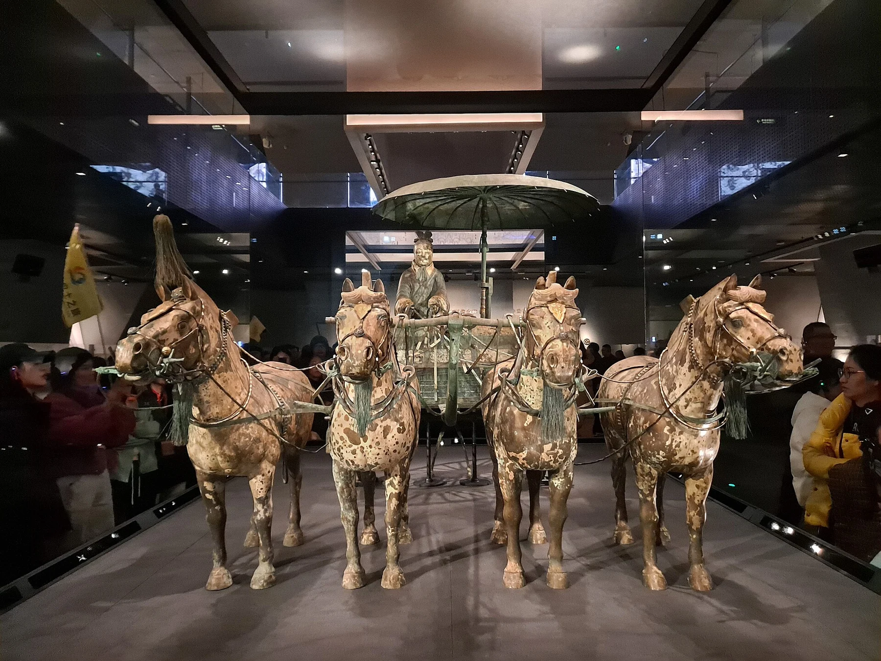 Four horses and an open bronze vehicle with a standing driver and umbrella