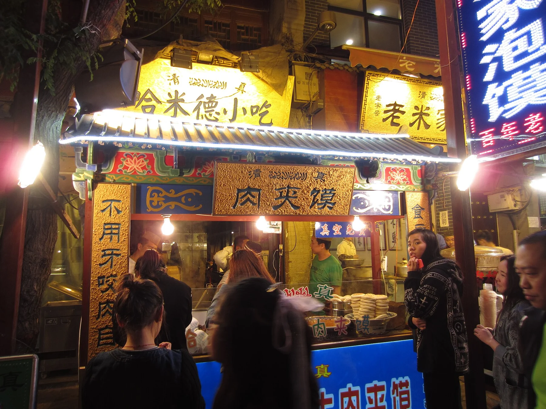 A shop front with a visible 肉夹馍 sign and people outside at night.