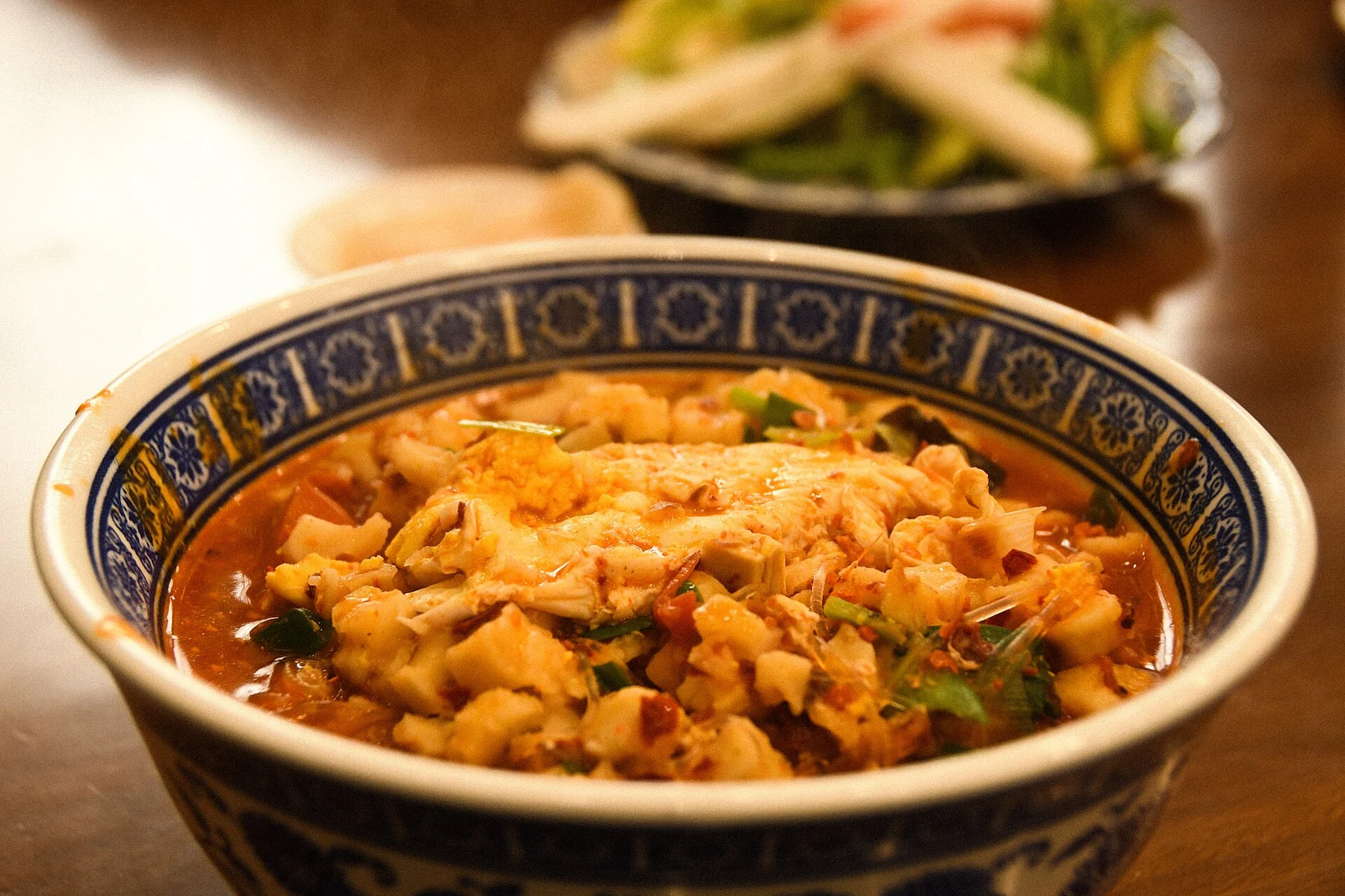 A bowl of paomo with bread pieces and meat, photographed on a table.