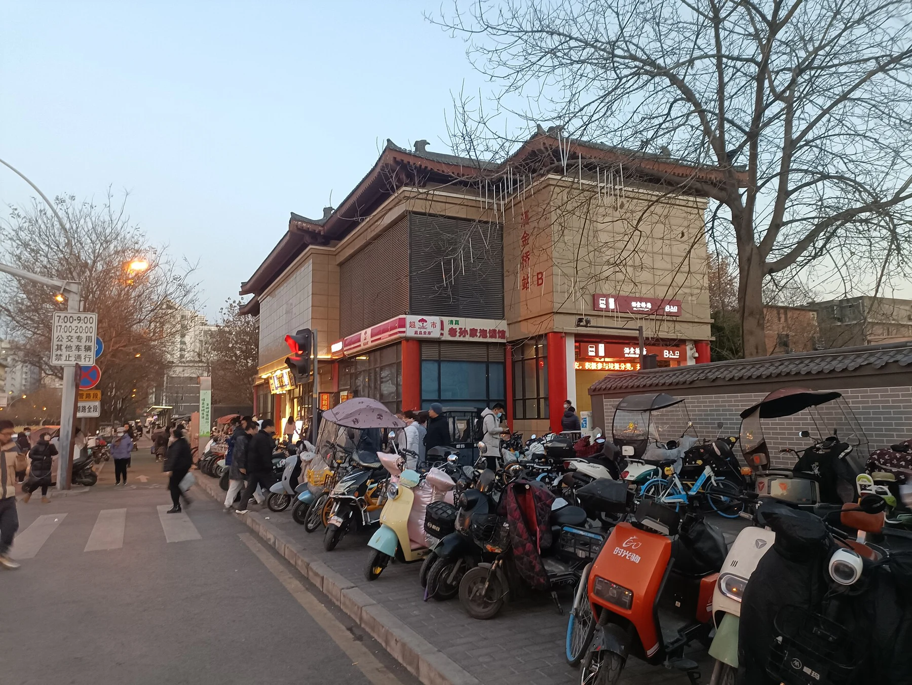 An older station-exit building beside parked scooters and pedestrians.