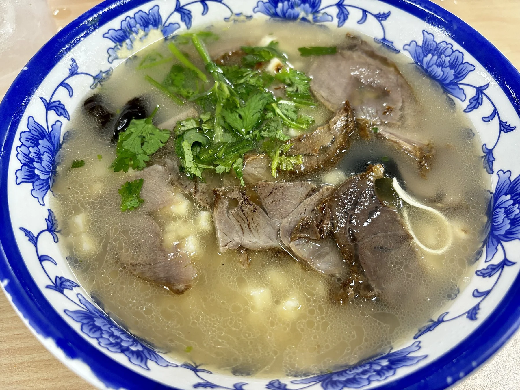 Beef slices, bread pieces and herbs in a blue-and-white bowl of paomo.