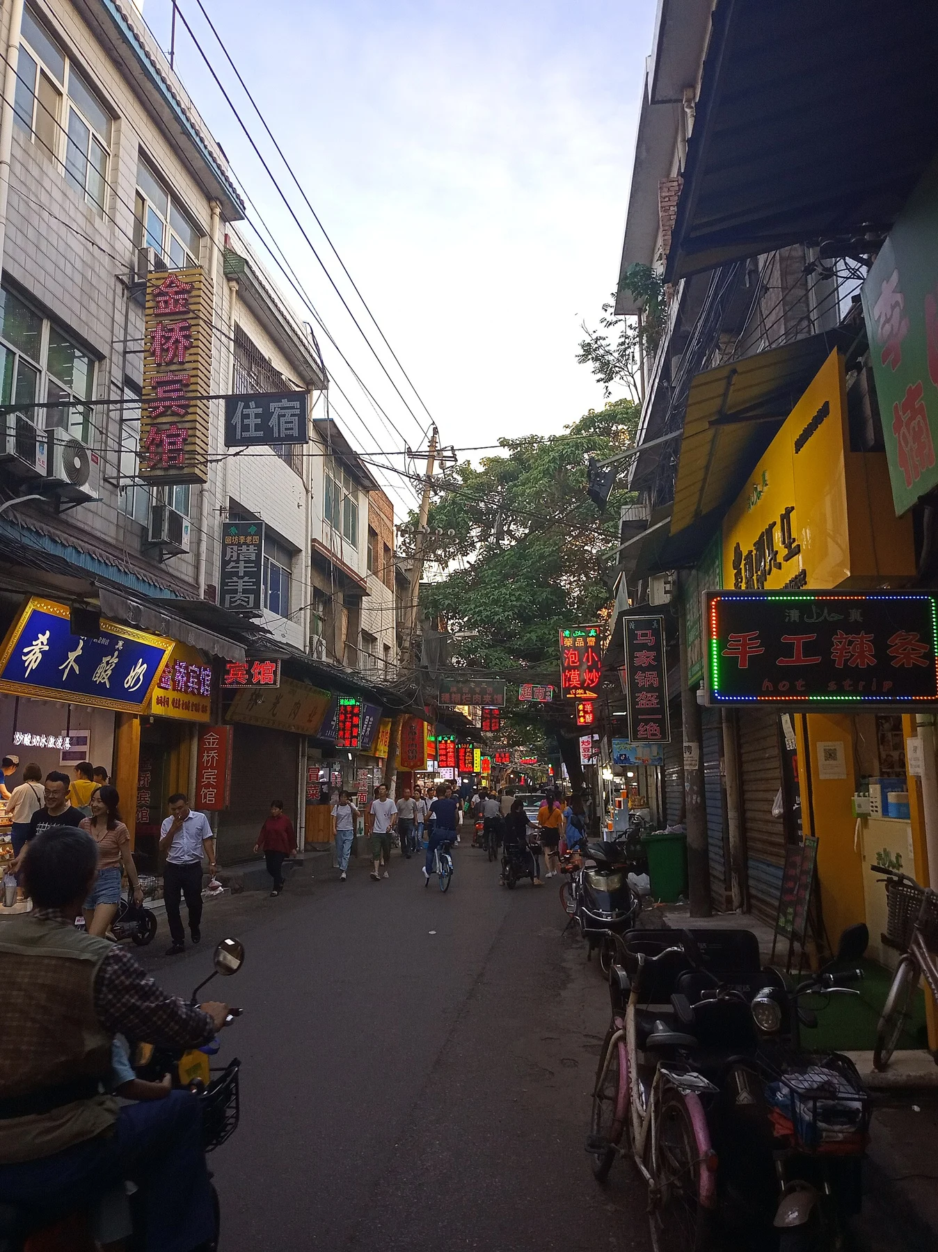 A narrow Sajinqiao streetscape lined with shops and people in daylight.