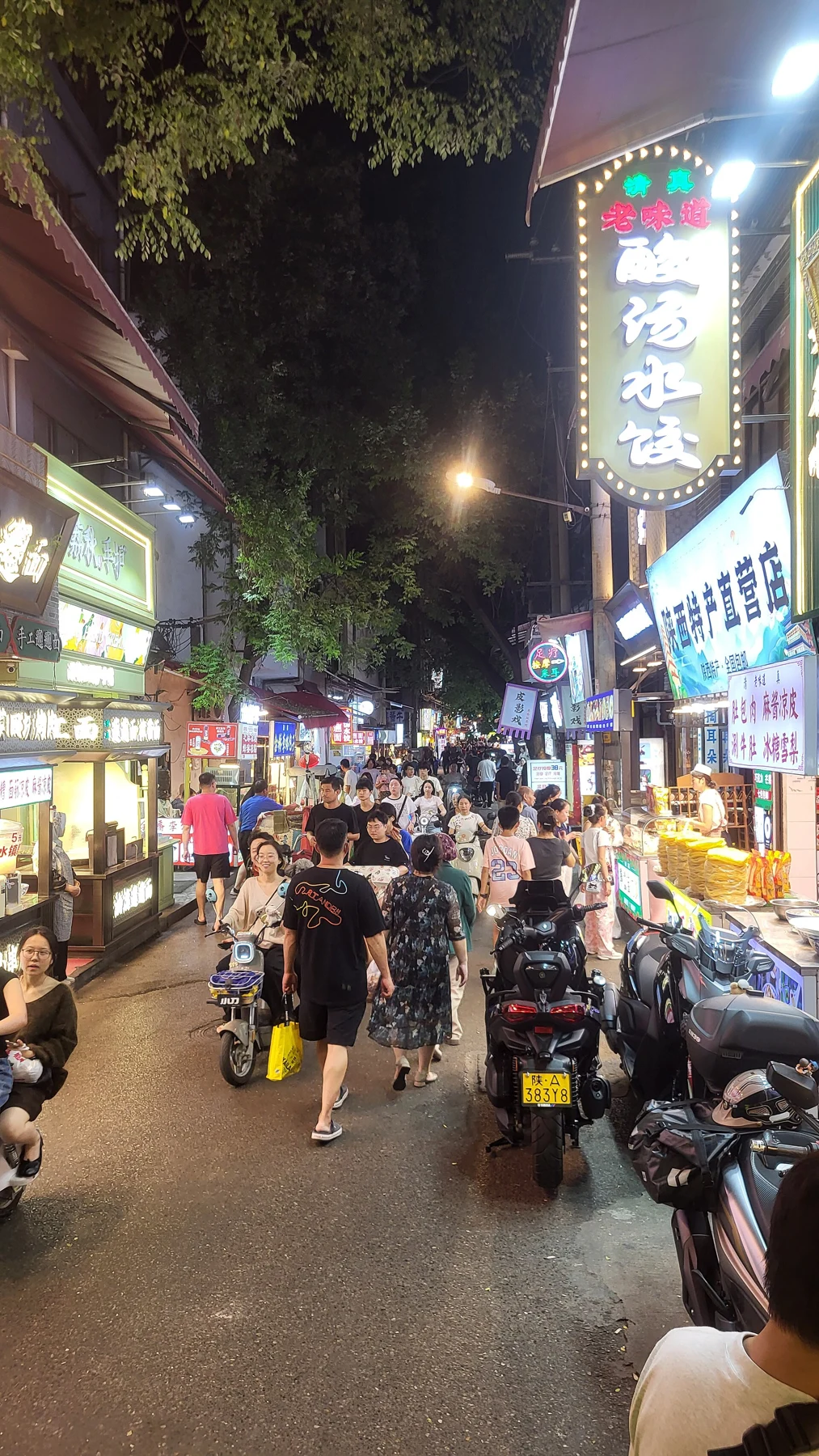 People and food-business signs on Sajinqiao at night.