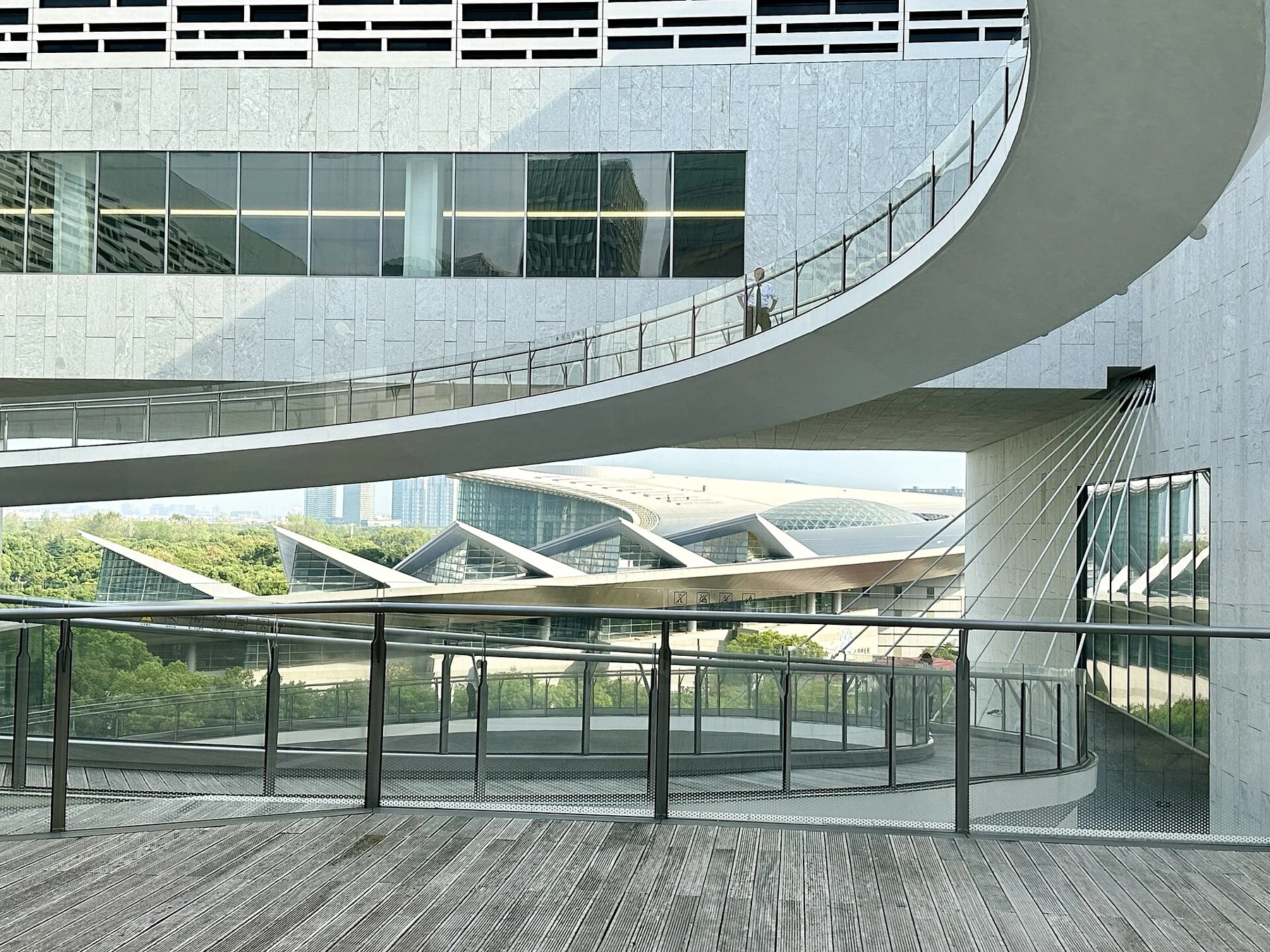 A museum balcony with glass railings, curved pale walls and diagonal roof members.