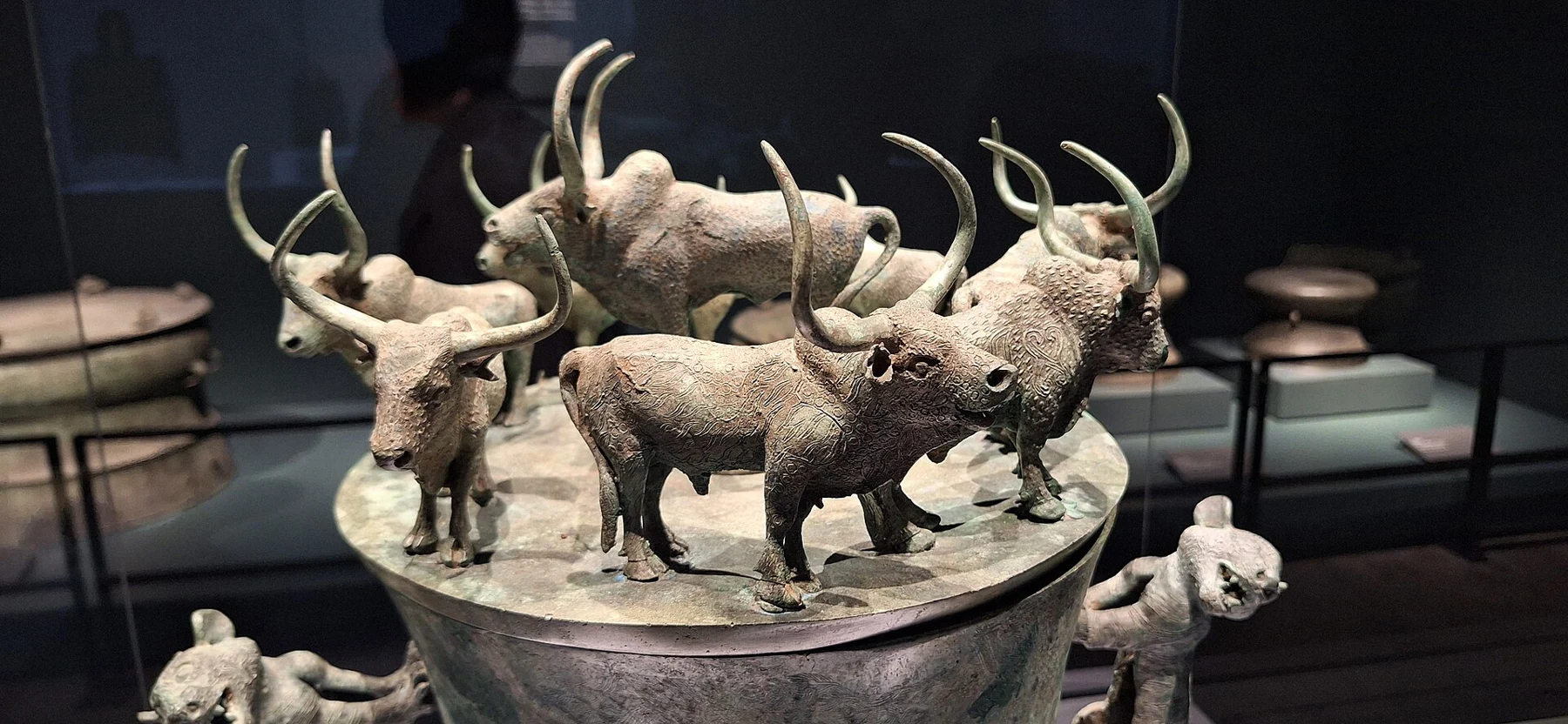 A close view of horned bovine figures standing on a circular bronze lid.