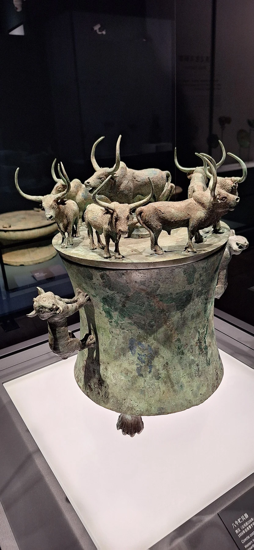 A waist-shaped bronze container with a large bovine and smaller cattle figures on its lid.