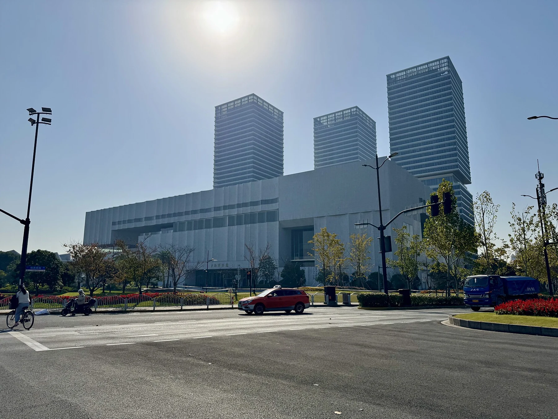 A broad pale modern museum building beside a road, with taller buildings behind it.