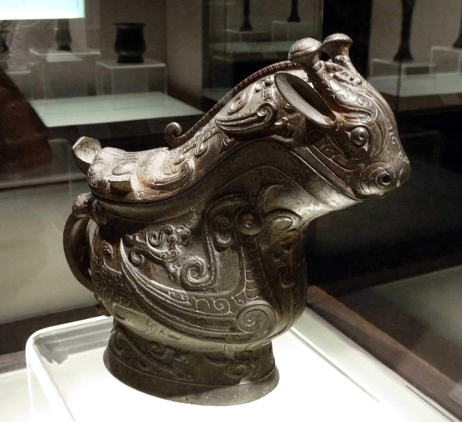 A side view of a bronze animal-headed wine vessel with a curved lid and patterned body.