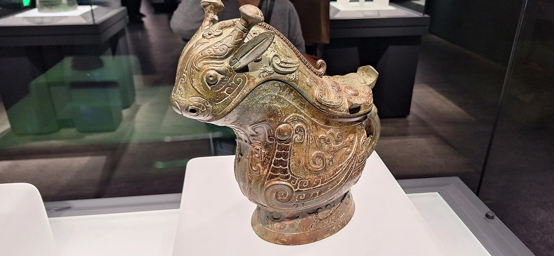 A bronze lidded wine vessel with a fantastical animal head and dense bird-and-creature decoration.