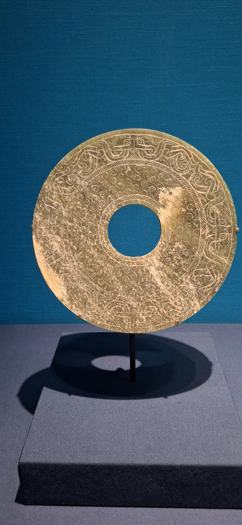 A circular carved disk with a central hole, standing vertically against a blue background.