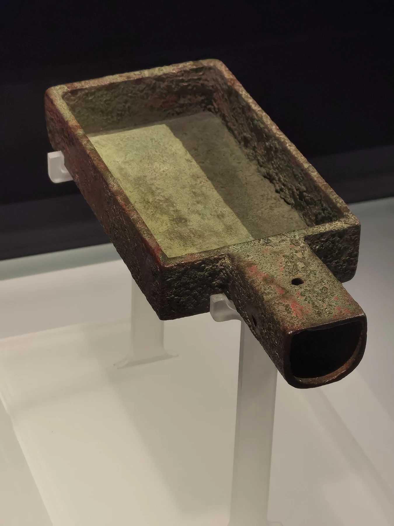 An oblique close view into a rectangular bronze vessel with incised marks and a short handle.