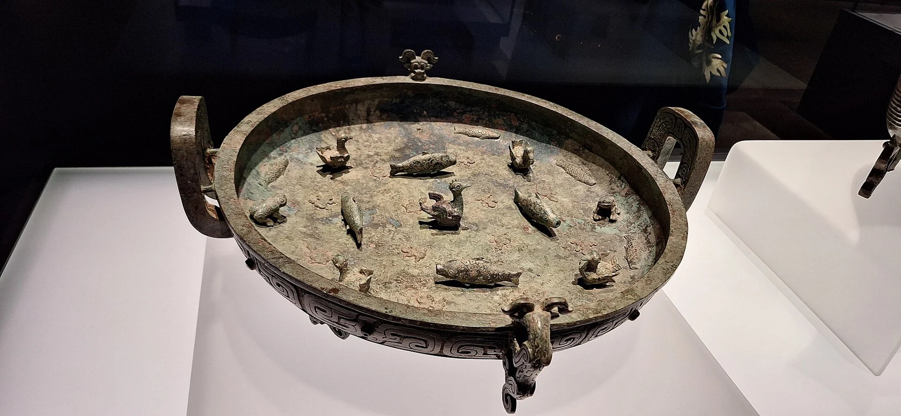 An angled view into a bronze basin with a central bird and rings of aquatic animal decoration.