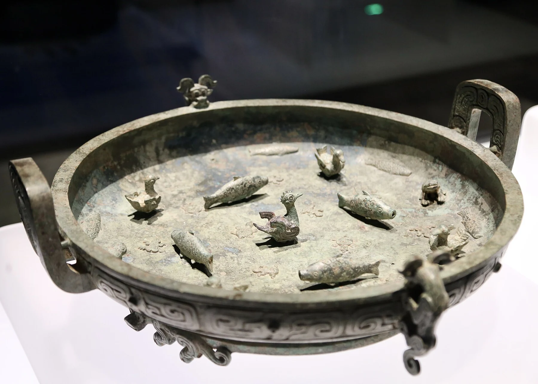 A shallow bronze basin with raised handles and small birds, fish, frogs and turtles arranged inside.
