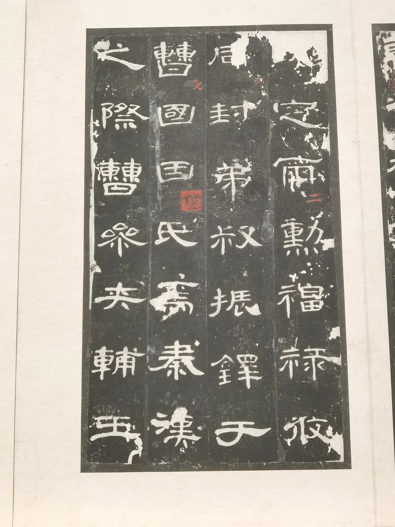 Pale Chinese characters against a dark rubbed surface, mounted on paper with collection marks.