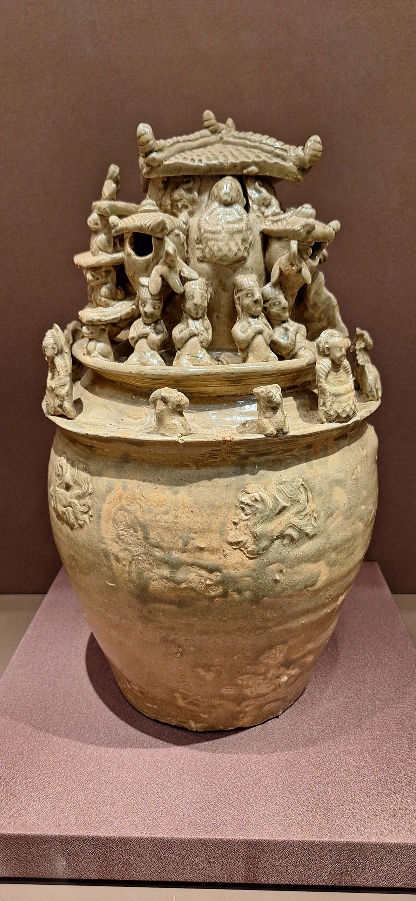 A glazed ceramic jar topped by a crowded miniature architectural and figural composition.