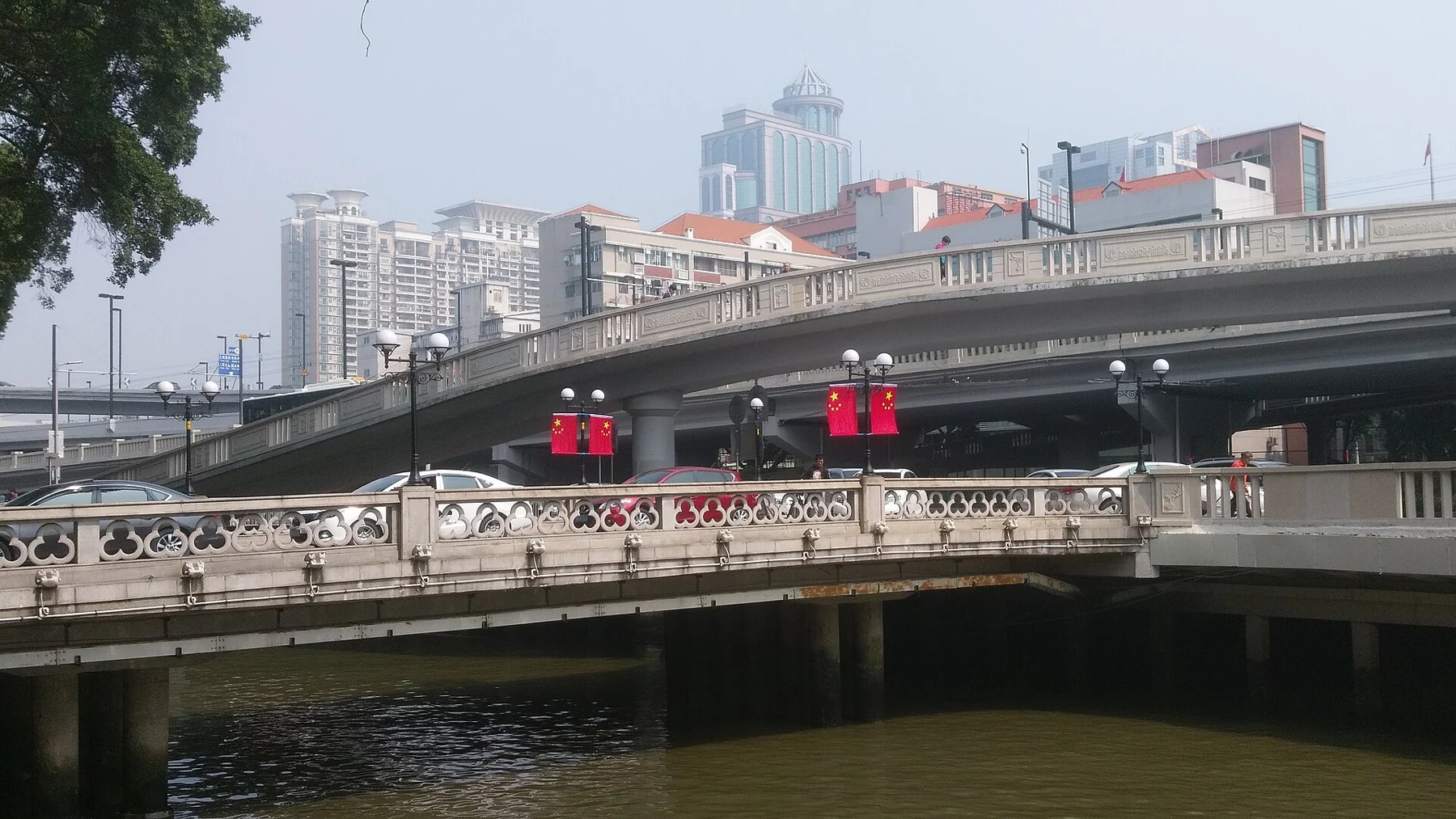 Low decorated bridge over the canal with road infrastructure and city buildings behind.