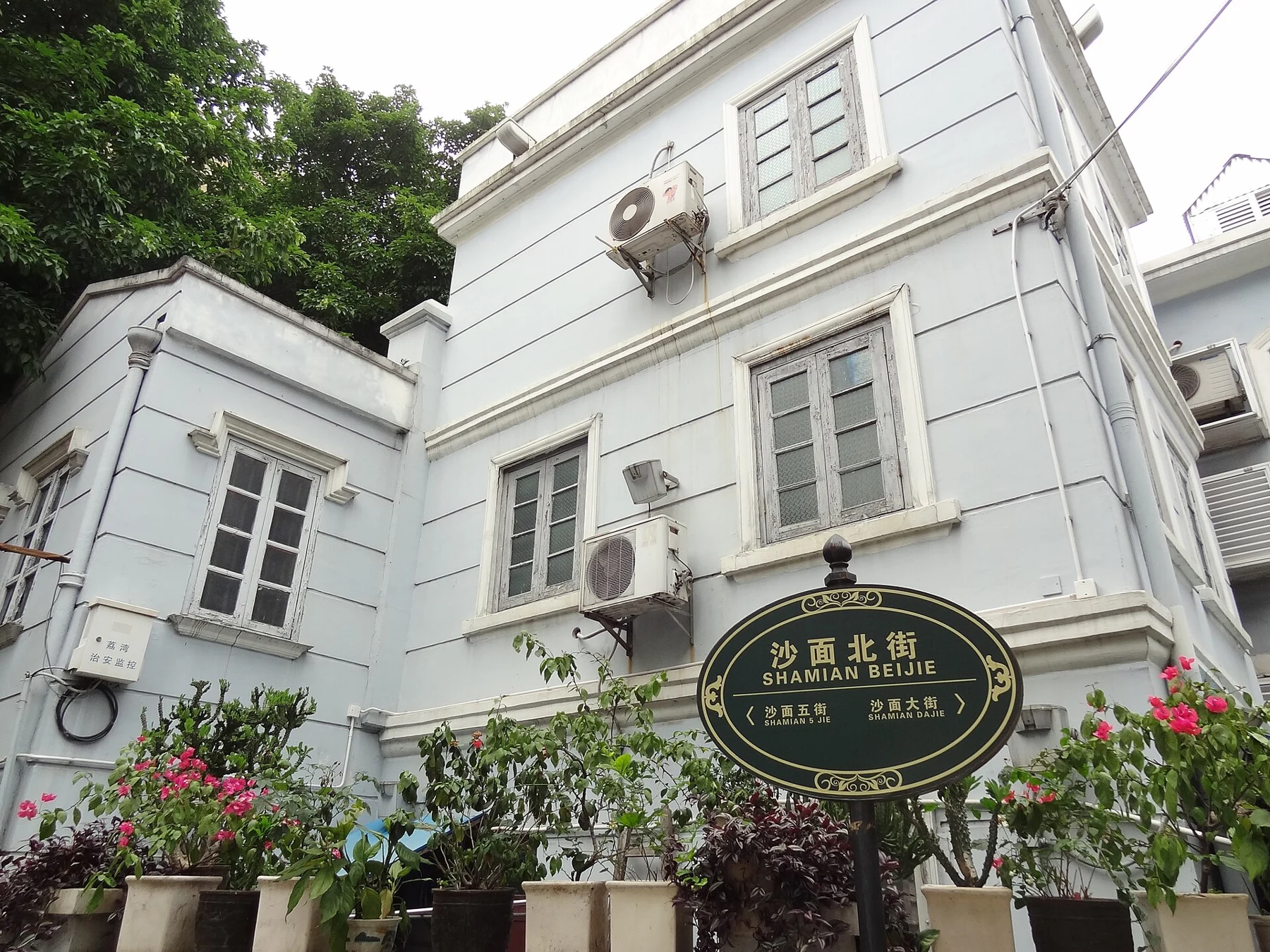 White building with shutters, flowers and a circular Shamian Bar and Library sign.