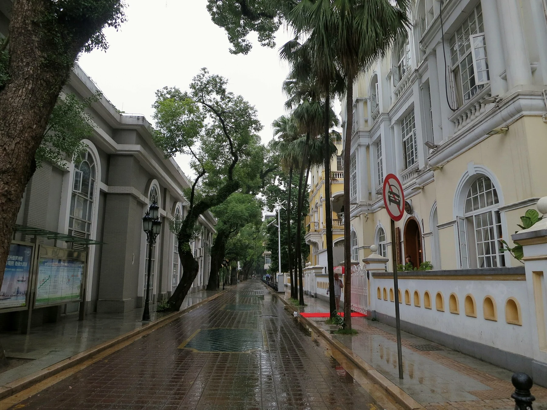 Narrow wet street between pale buildings and trees in Shamian.