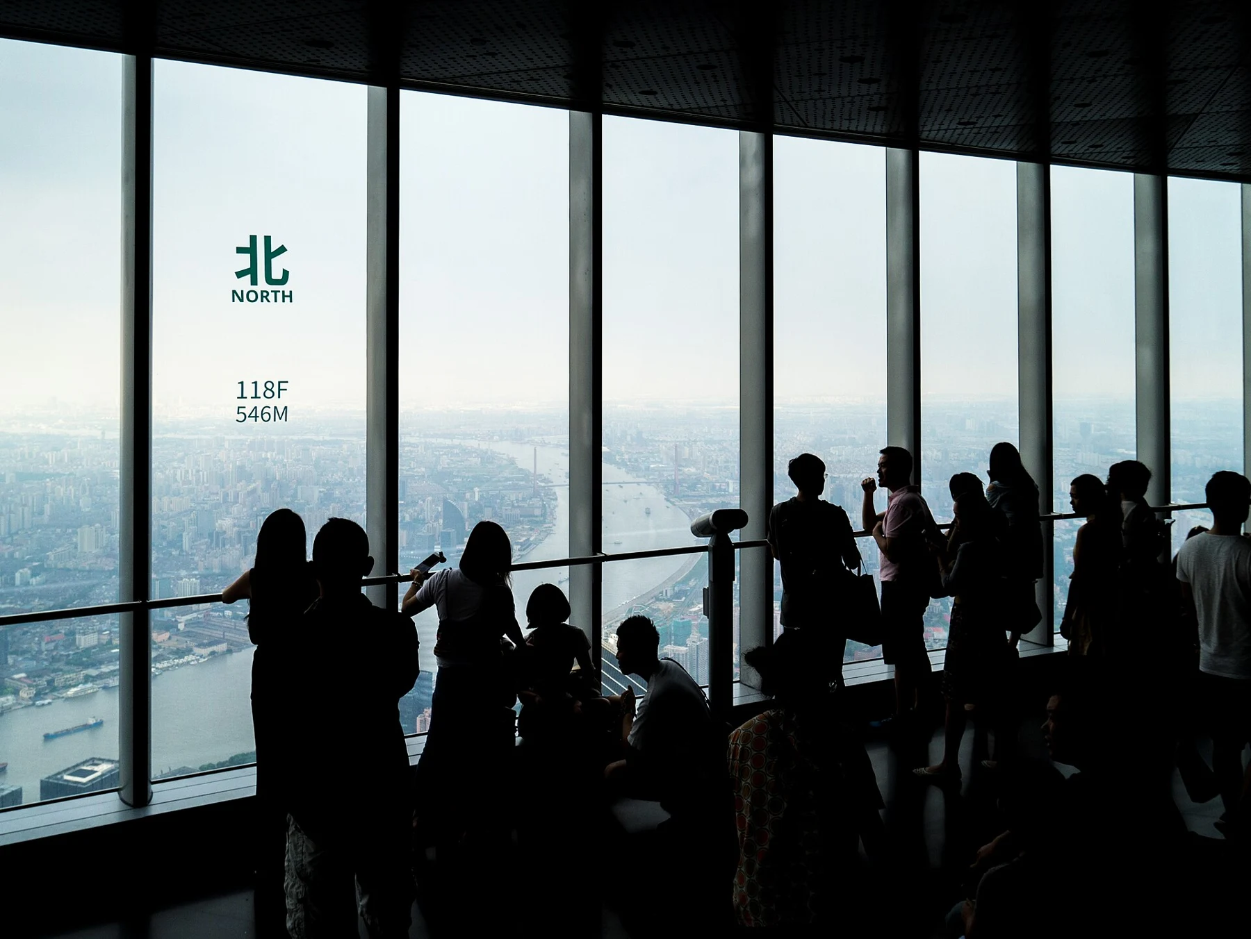 Visitors inside the glazed viewing area beside the north direction and 118F sign.