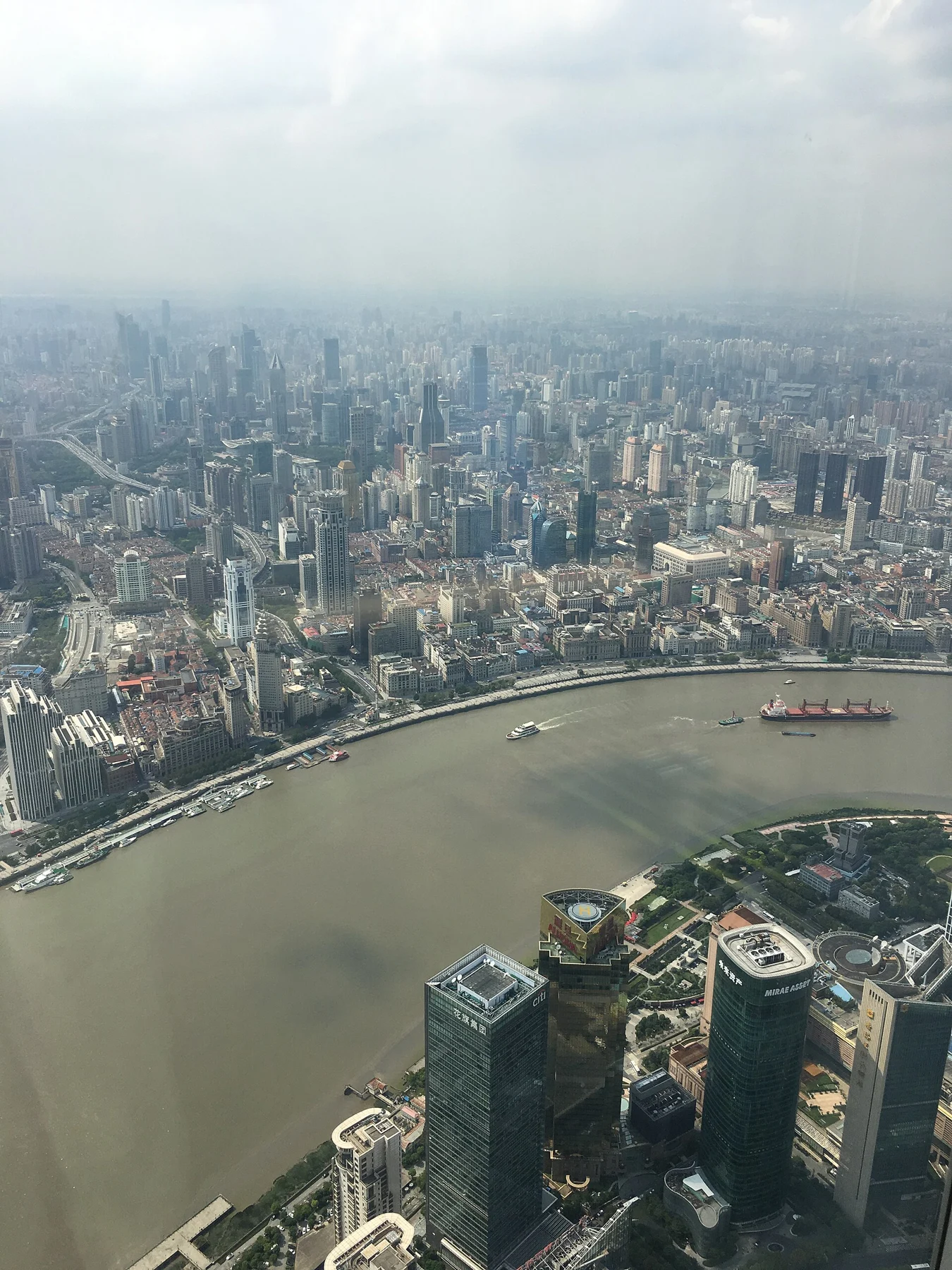 Huangpu River bend with riverside buildings and a hazy city beyond.
