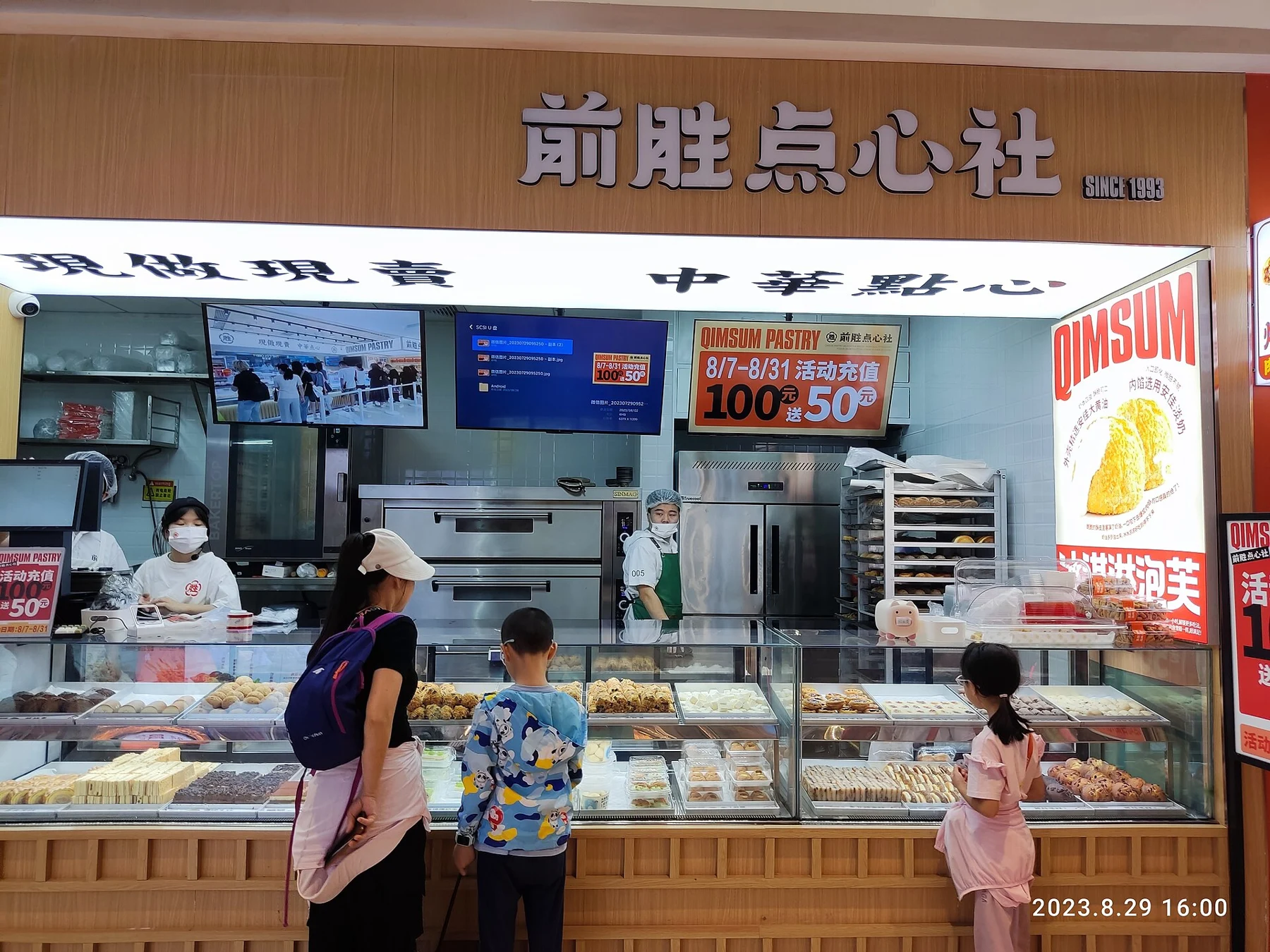 People beside a glass-fronted dim sum counter and a Chinese shop sign.