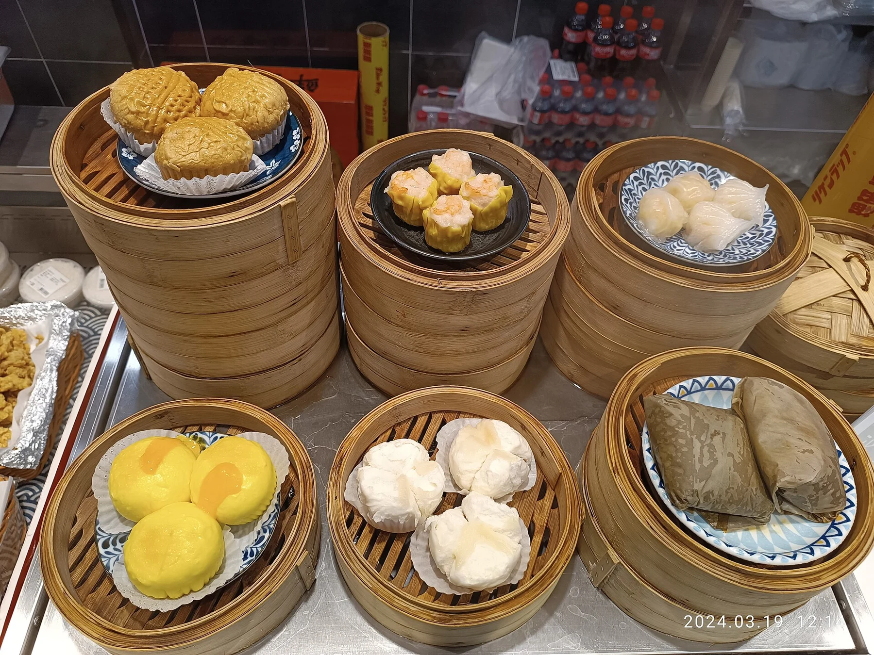 A food-counter display of buns, dumplings and leaf-wrapped parcels on bamboo steamers.