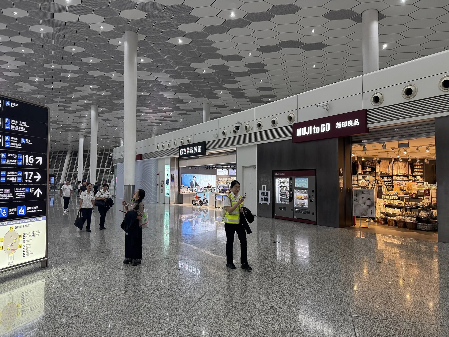 Airport ground transportation hall with shops, people and directional signs in October 2026.