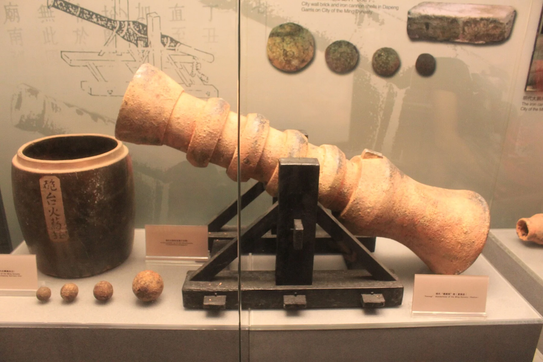 Metal cannon barrel on a black stand beside a jar and several round shot