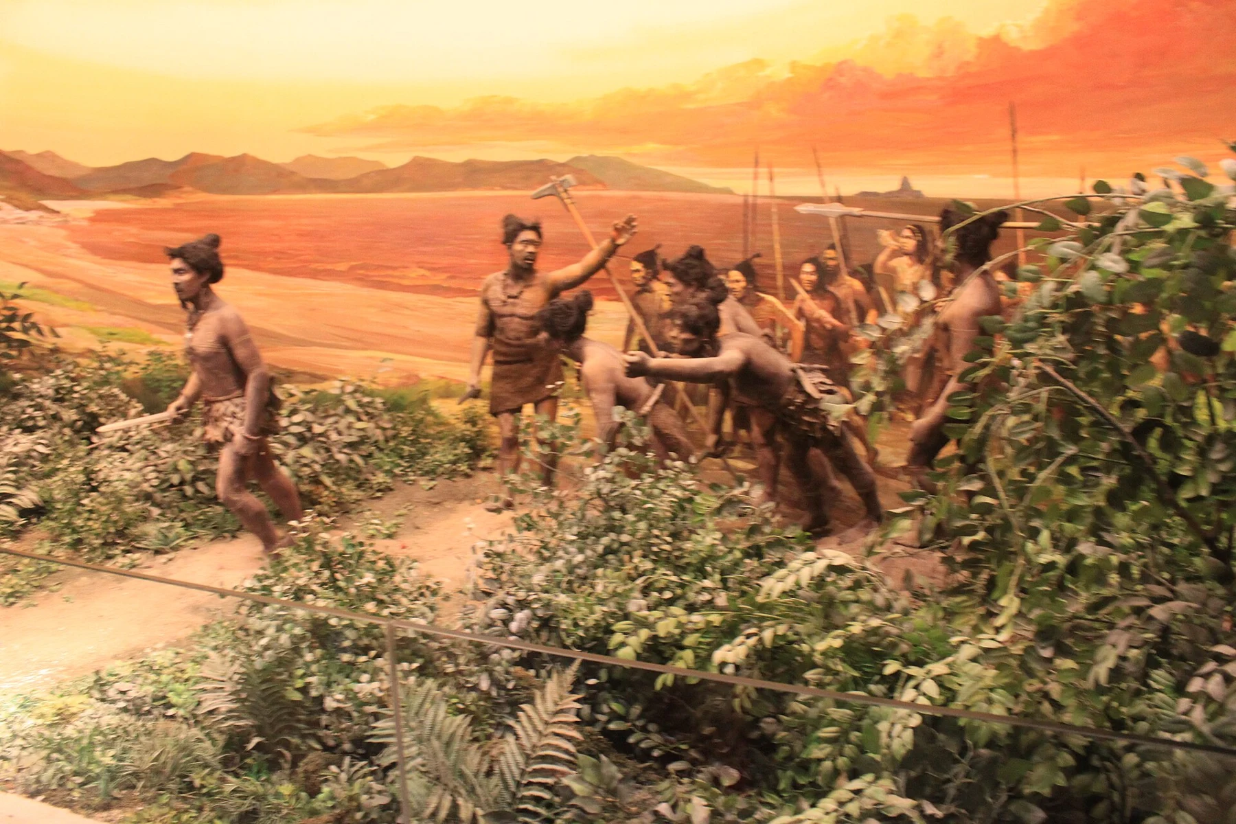 Human figures carrying tools against a painted coastal background in a museum diorama