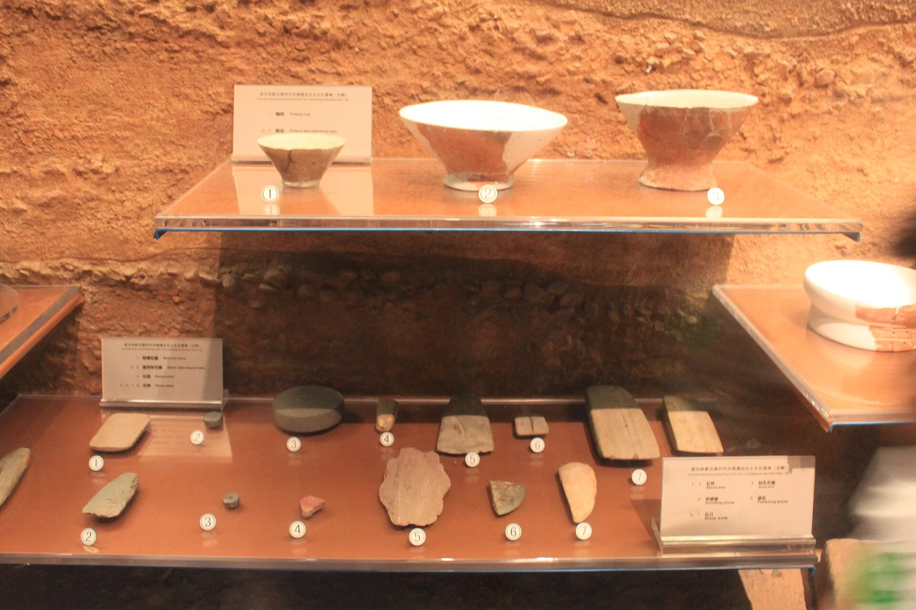 Pottery bowls above flat and rounded stone implements with bilingual labels