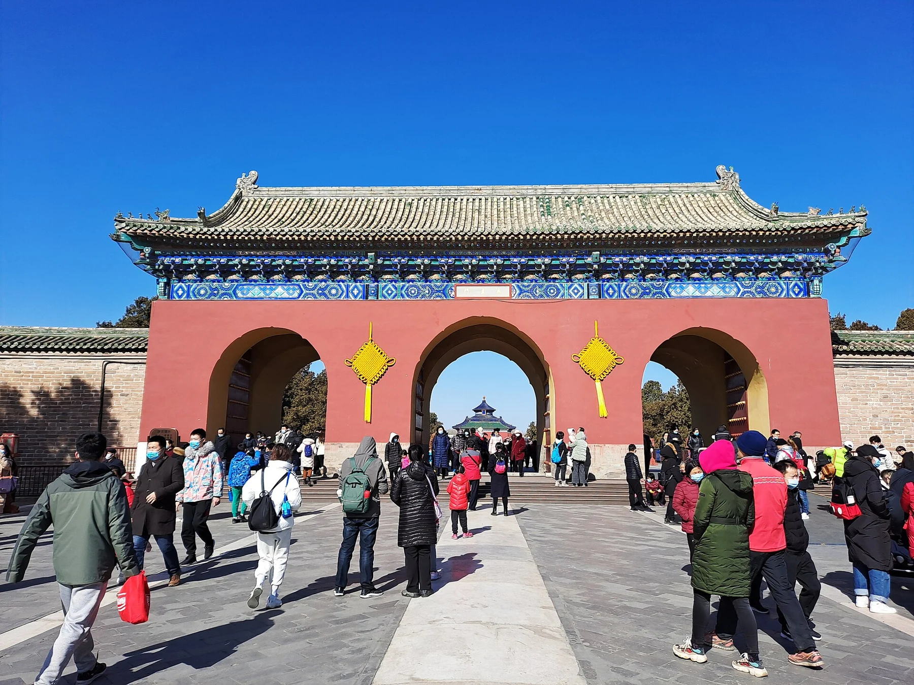 A red triple-opening ceremonial gate on the Danbi Bridge approach, with the Hall of Prayer visible in the distance.