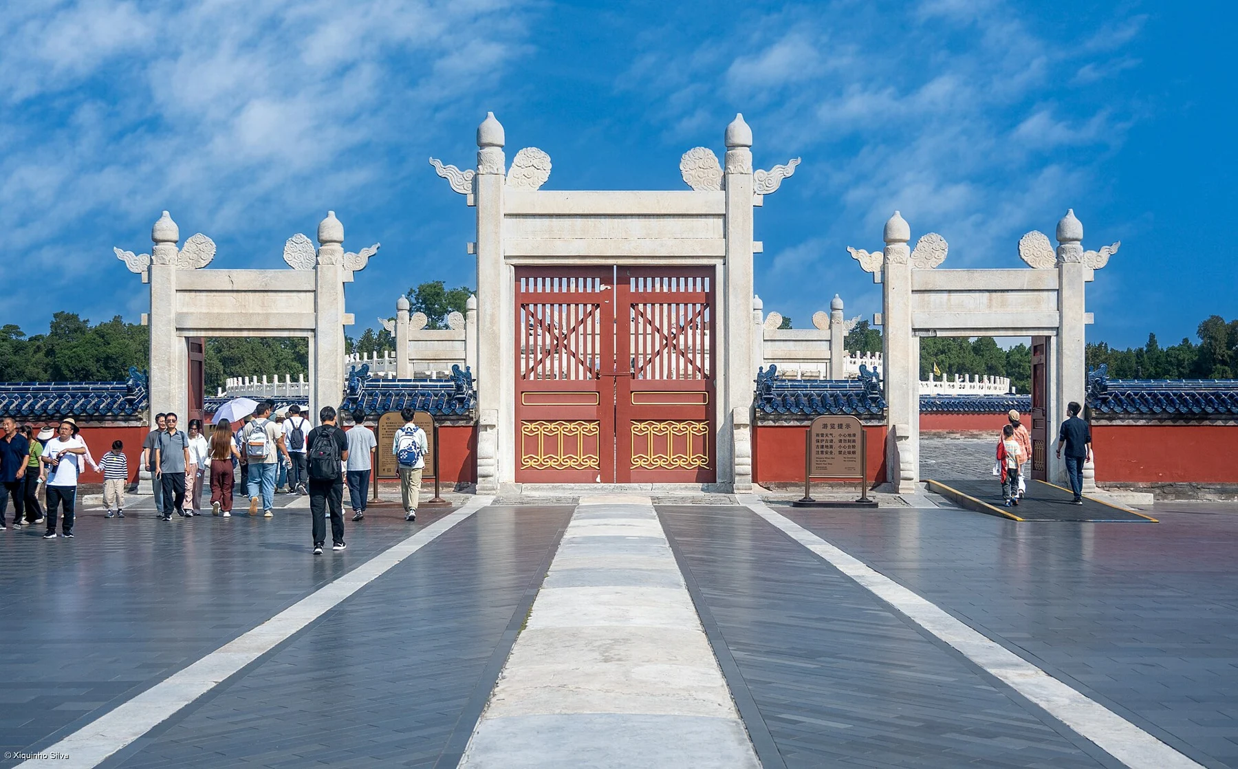 Three openings of a white ceremonial gate, with red doors and visitors passing through.